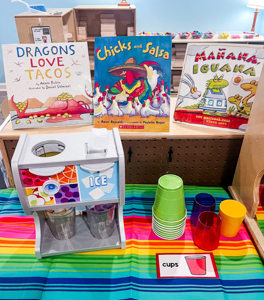 Books displayed with cups and a pretend drink machine in a taco dramatic play center.