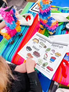Preschool student pointing at a menu in a taco dramatic play center.