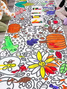 Preschoolers coloring a large Friends Art Lab banner with paint sticks during a group art activity.