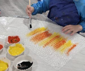 Preschooler painting bubble wrap with yellow paint for a honeycomb-themed art activity.