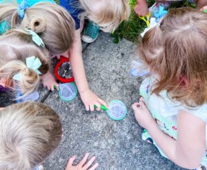 Preschool students use magnifying glasses to closely inspect insects in an outdoor setting. hands-on insect activities
