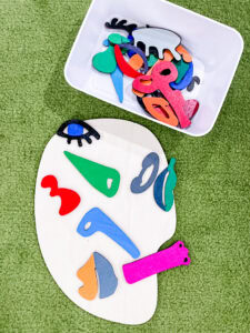 A white face cutout arranged with colorful puzzle pieces to resemble an abstract Picasso-style face, created by a preschool student.