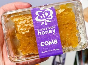 Preschool teacher holding a clear container of raw honey with visible honeycomb inside.