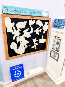 White felt pieces arranged on a black felt board with It Looked Like Spilt Milk displayed on a shelf below.