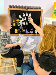 Preschool teacher and child pointing at felt board pieces from Ten Timid Ghosts while the child holds the open book.