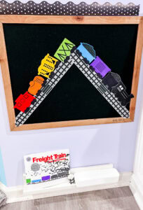 Black felt board with colorful train cars on a track; Freight Train book displayed on a shelf below.