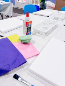 Art supplies including canvas, tissue paper, and glue set out on a table