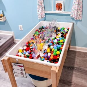 Preschool sensory bin filled with colorful pom poms and clear plastic vases for sorting.