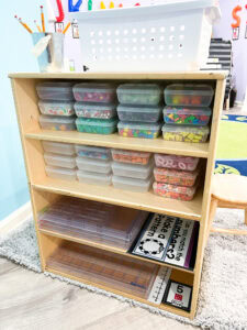 Back view of a preschool math center shelf filled with clear plastic bins of colorful math manipulatives and activity cards.