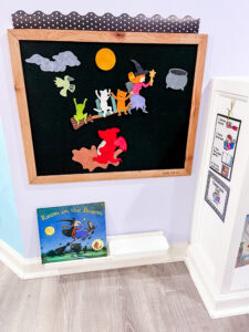 Felt board display for Room on the Broom, showing felt characters riding on a broomstick with a moon, clouds, and dragon, alongside the book below.