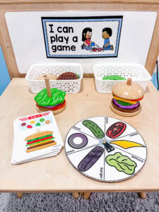 Preschool math center with burger building game, ingredient spinner, order cards, and play food pieces.
