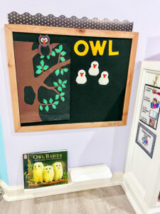 Felt board display for Owl Babies with a tree, three baby owls, a parent owl, and the word “OWL” in yellow letters, alongside the book below.