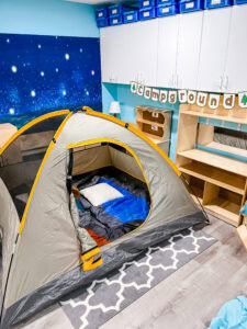 Indoor classroom camping center with a full-size tent, sleeping bags, and a “Campground” banner.