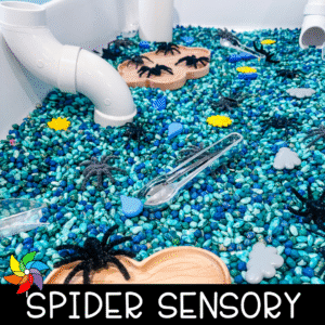 Close-up of a preschool sensory bin filled with blue and green dyed beans, plastic spiders, weather-themed pieces, tongs, and PVC pipes.