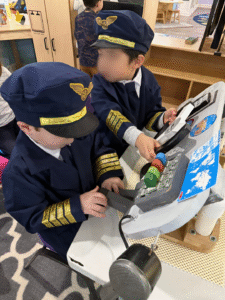 Preschoolers dressed as pilots role-playing in a dramatic play airplane center.