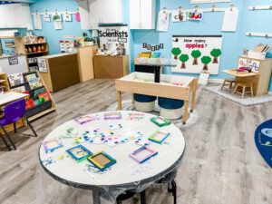 Preschool classroom with learning centers including art, sensory, literacy, and science areas arranged for free choice play.