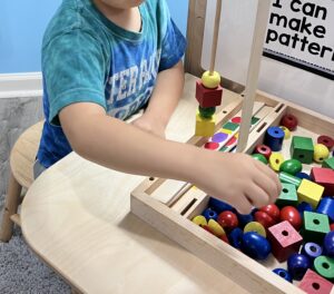 Preschool child creating patterns with colorful wooden beads