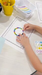 Child placing colorful star stickers along a letter tracing page for a preschool fine motor activity.