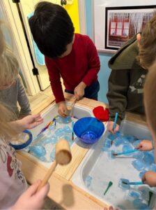 Ice cube sensory table with tools, bowls, and water for preschool winter science exploration.