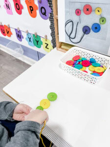 Child threading large buttons onto a plastic canvas using yarn as a fine motor lacing activity.
